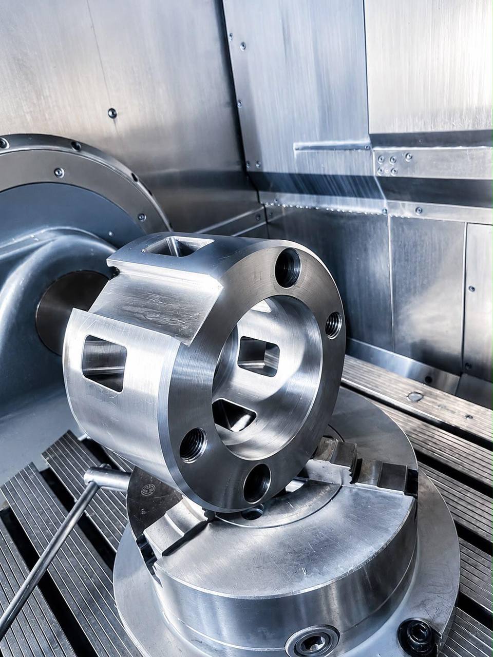 A finished steel housing held in a three-jaw chuck, with machined bores, threads and pockets on every face.